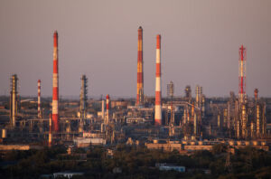 Industrial refinery complex with tall red-and-white striped smokestacks, pipelines, and processing towers at dusk